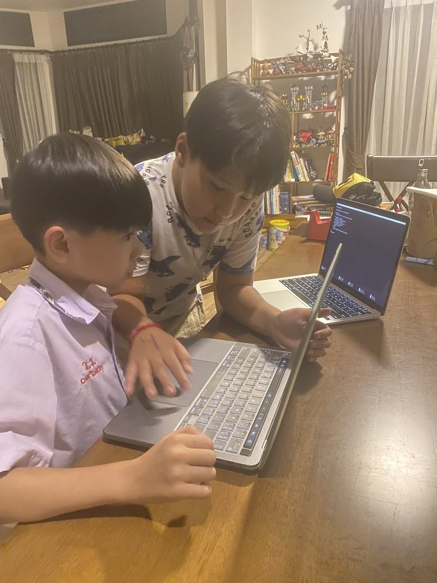 Two students collaborating on laptops with code editor in background