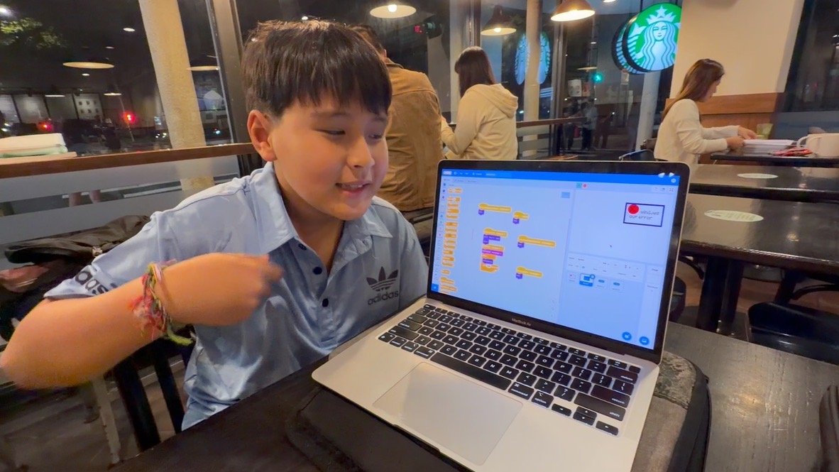 Young student proudly presenting his Scratch coding project on his MacBook